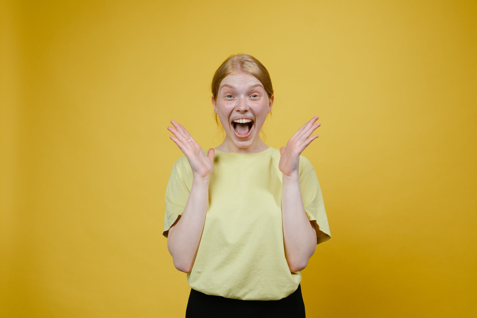 A woman in a yellow shirt is making a surprised face.