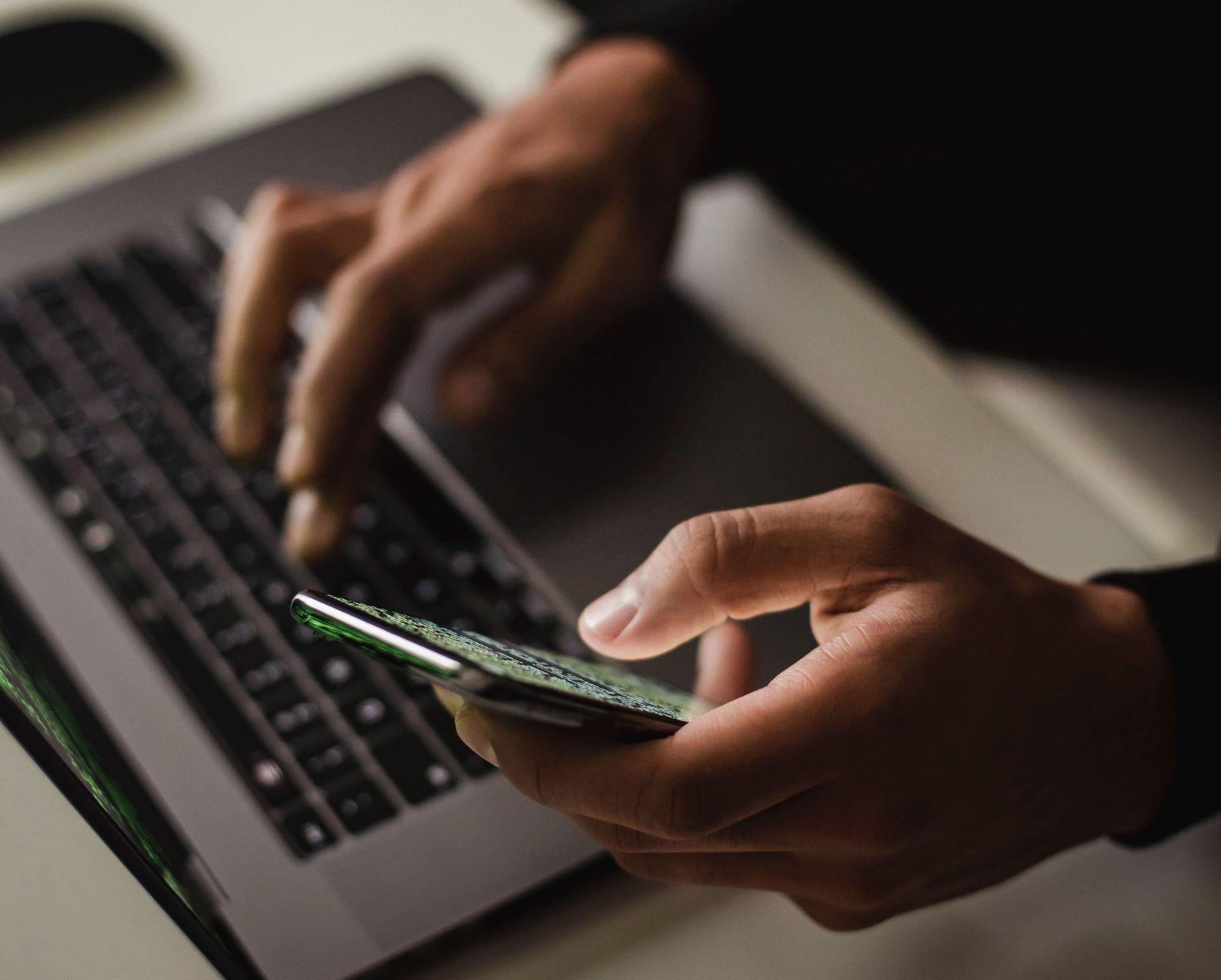 Person using a laptop and a smartphone simultaneously indoors.