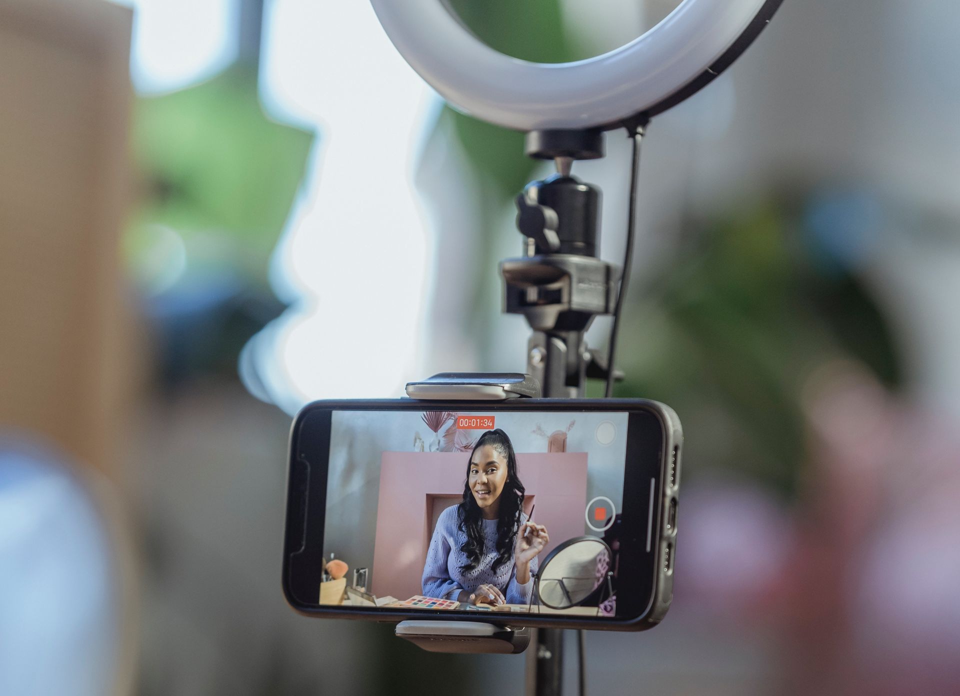 Close up phone recording user generated video content A woman is being filmed on a cell phone with a ring light attached to it.