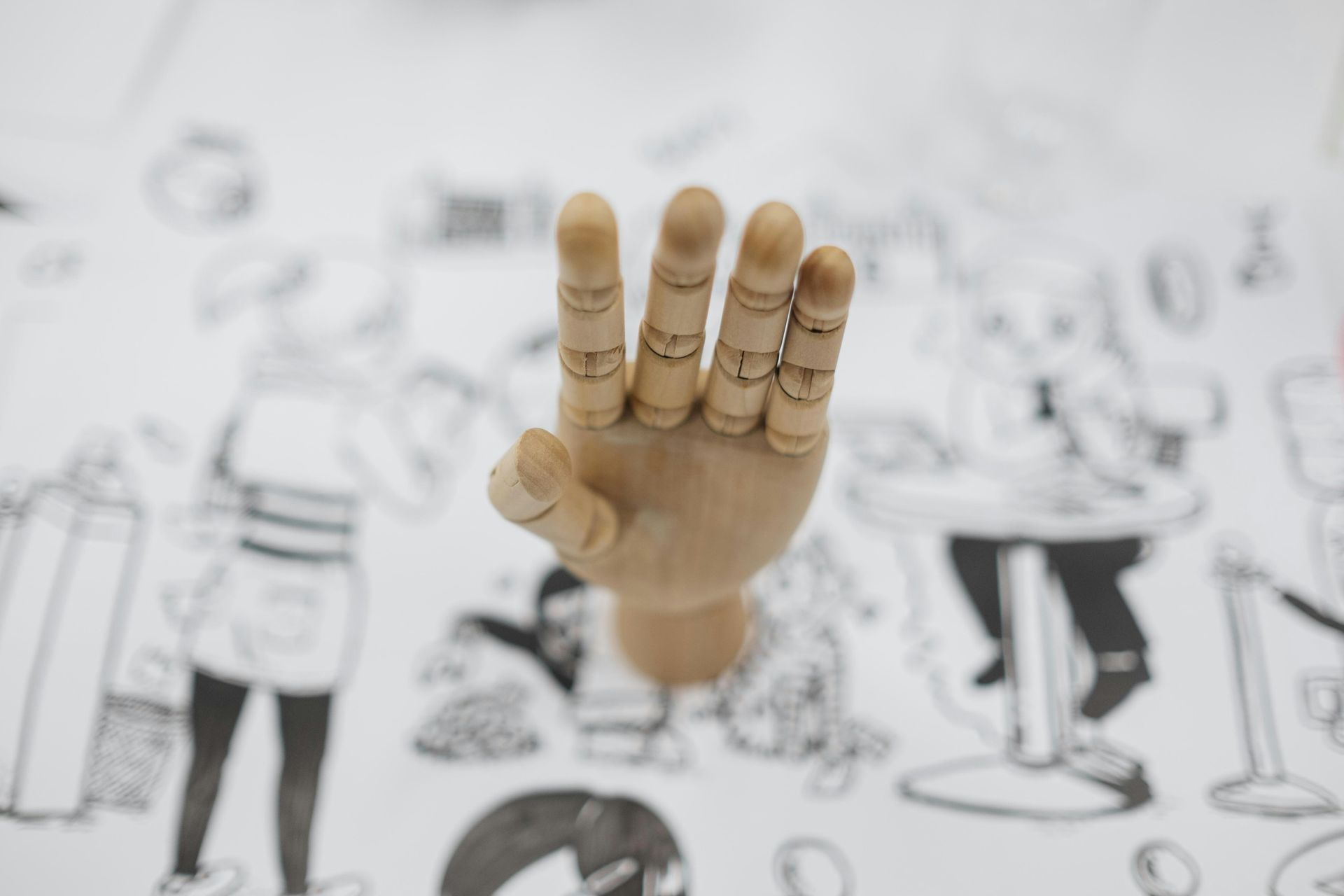 Wooden hand model displaying four fingers on a table with a black and white illustrated design. Wooden hand model displaying four fingers on a table with a black and white illustrated design.