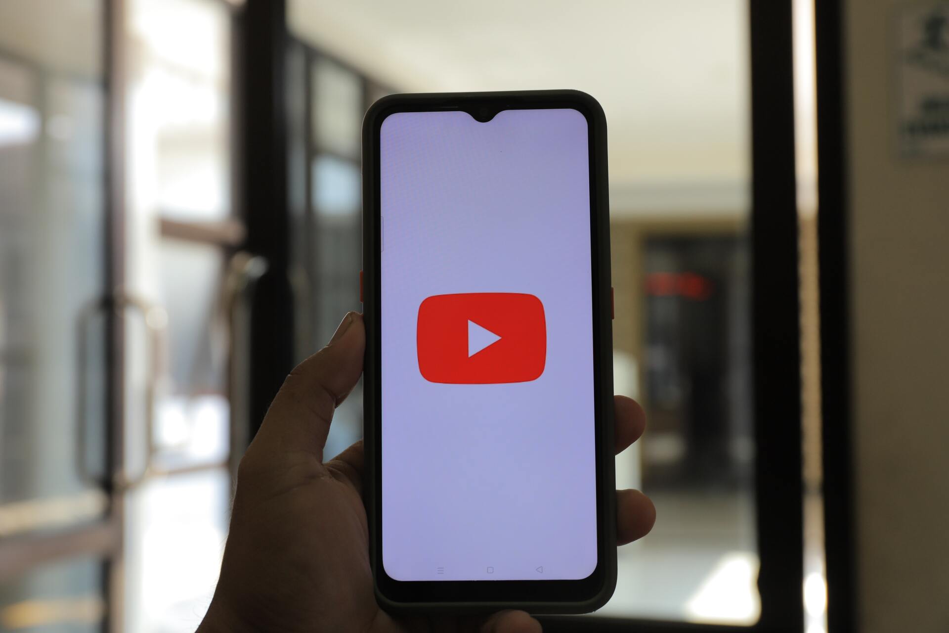 A person is holding a cell phone with a youtube logo on the screen.