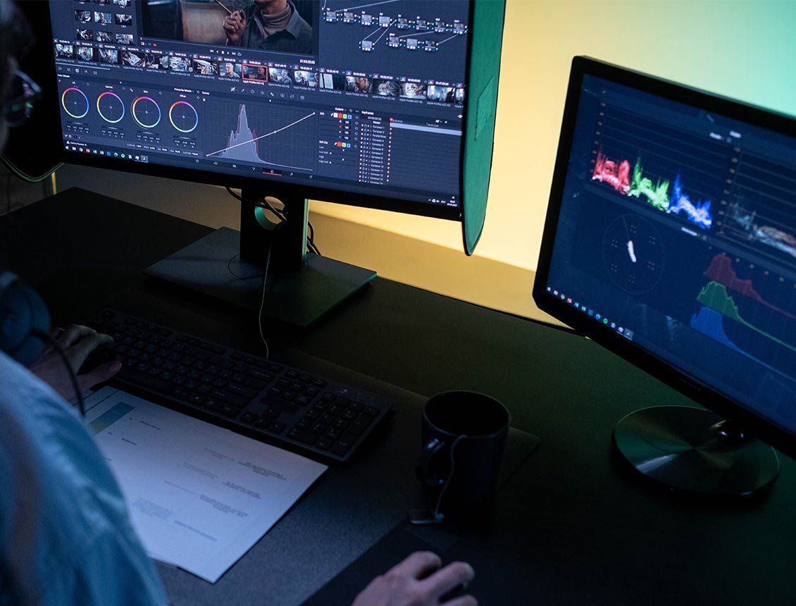 close up video editing workstation monitors A man is sitting at a desk using two computer monitors