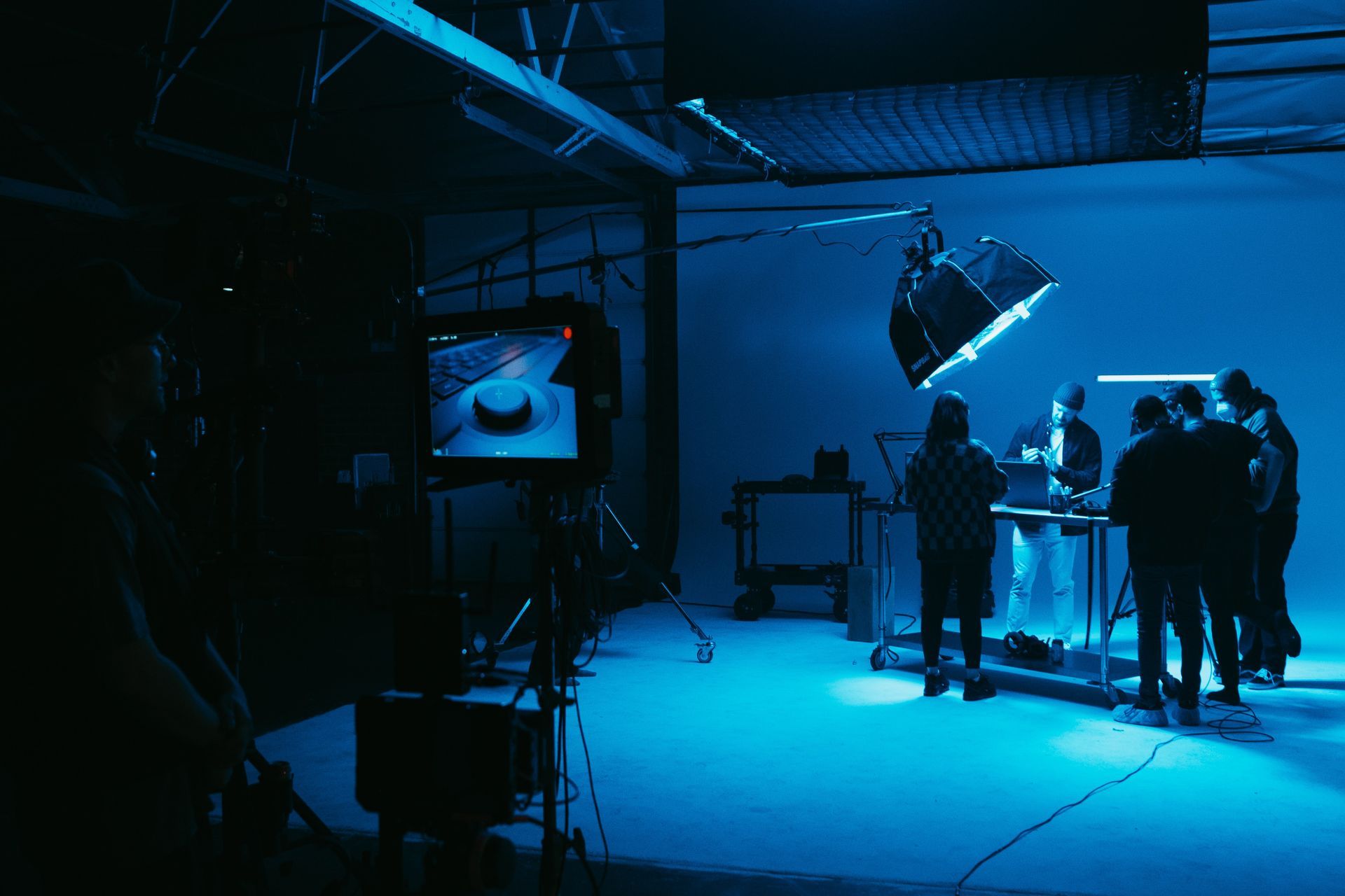 Studio film shoot with crew working on set dressing and blue wash lighting A group of people are standing in a dark blue studio.