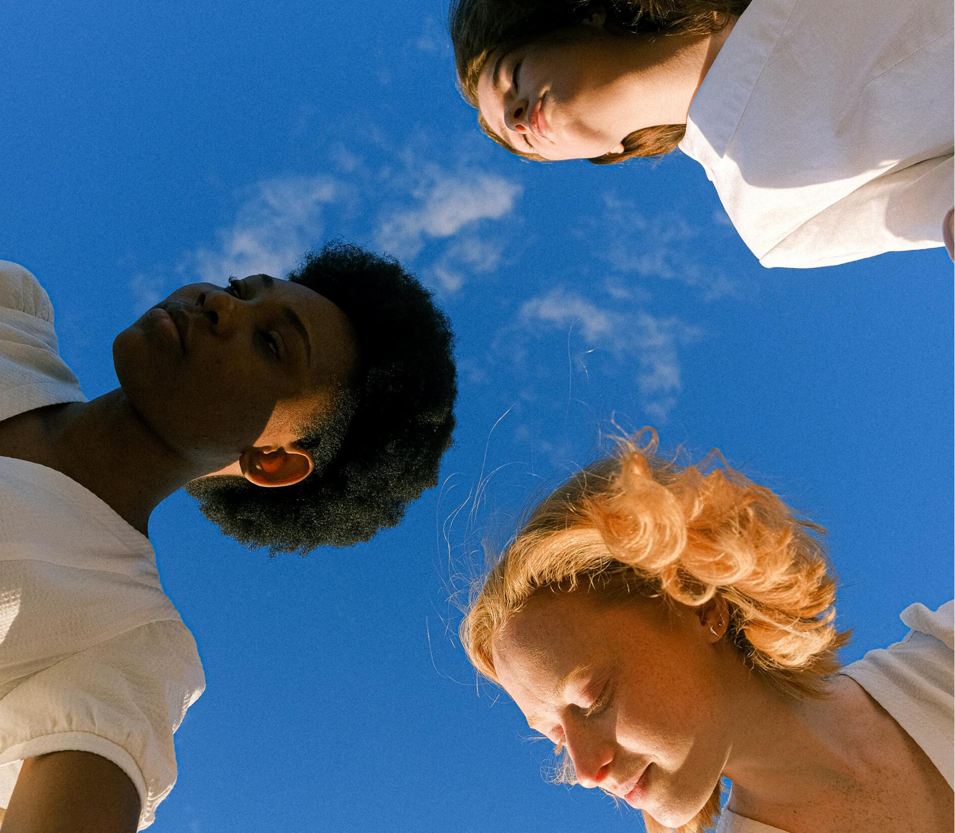 Looking up at the sky three faces pose with neutral expressions Three women are looking up at a blue sky