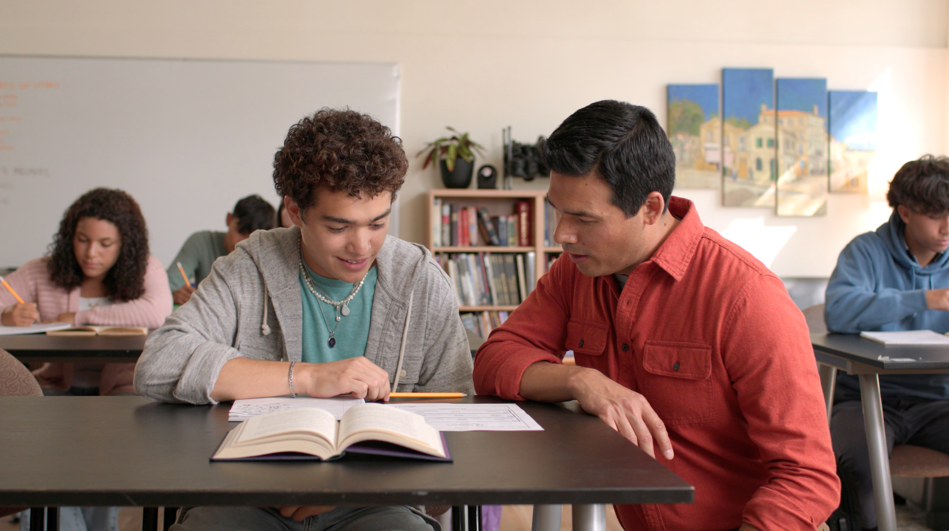 Student with curly hair and an adult reviewing papers in a classroom.