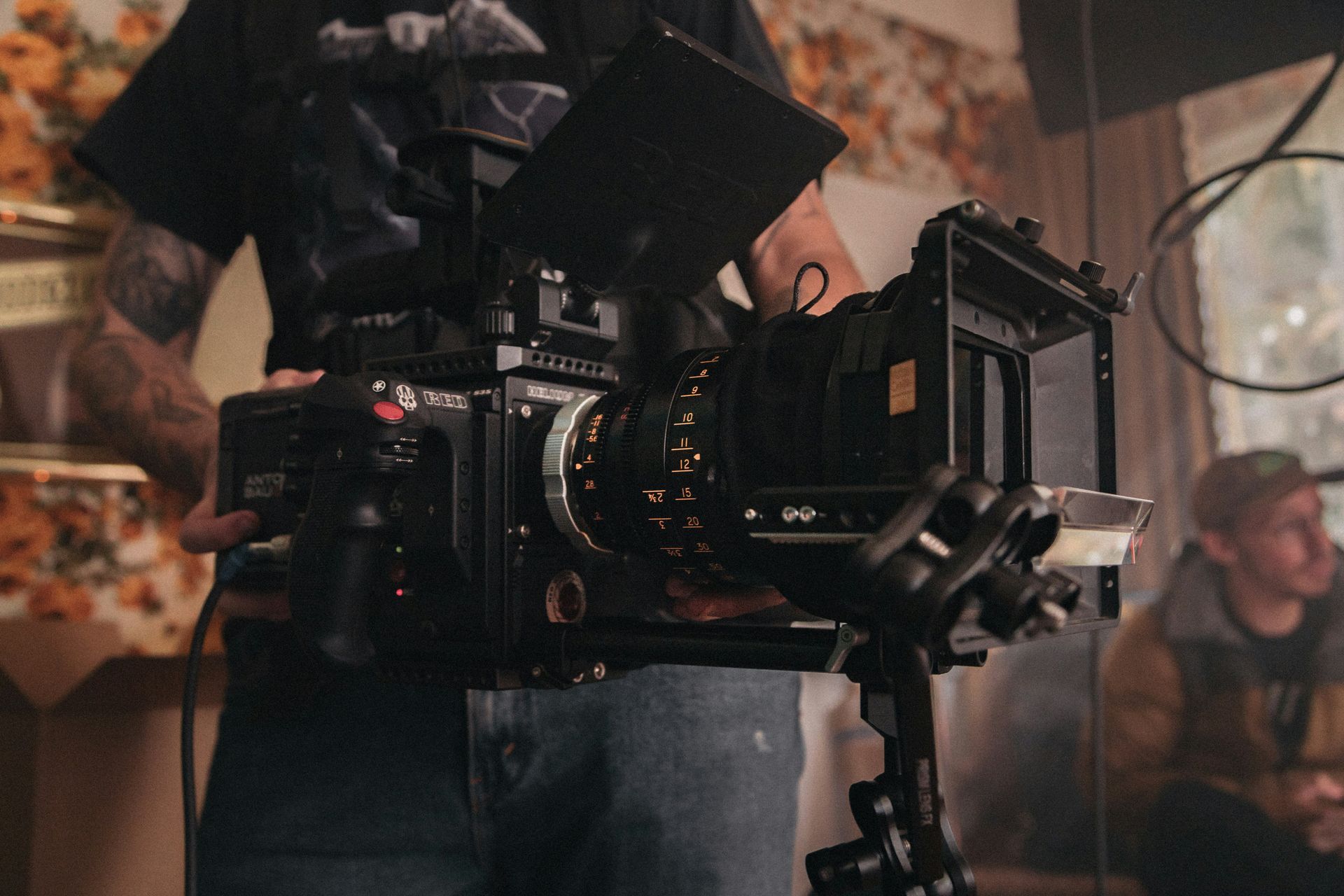 Behind the scenes close up image of a RED cinema camera operated by a camera person Person holding a large black video camera, filming inside a room.