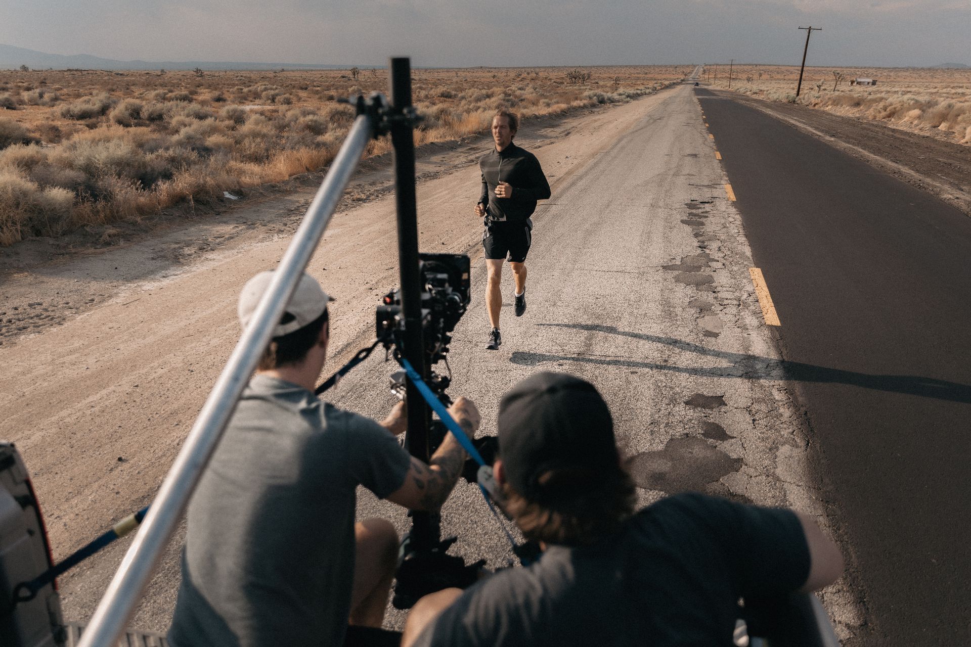A man is running down a dirt road while a cameraman takes a picture of him.