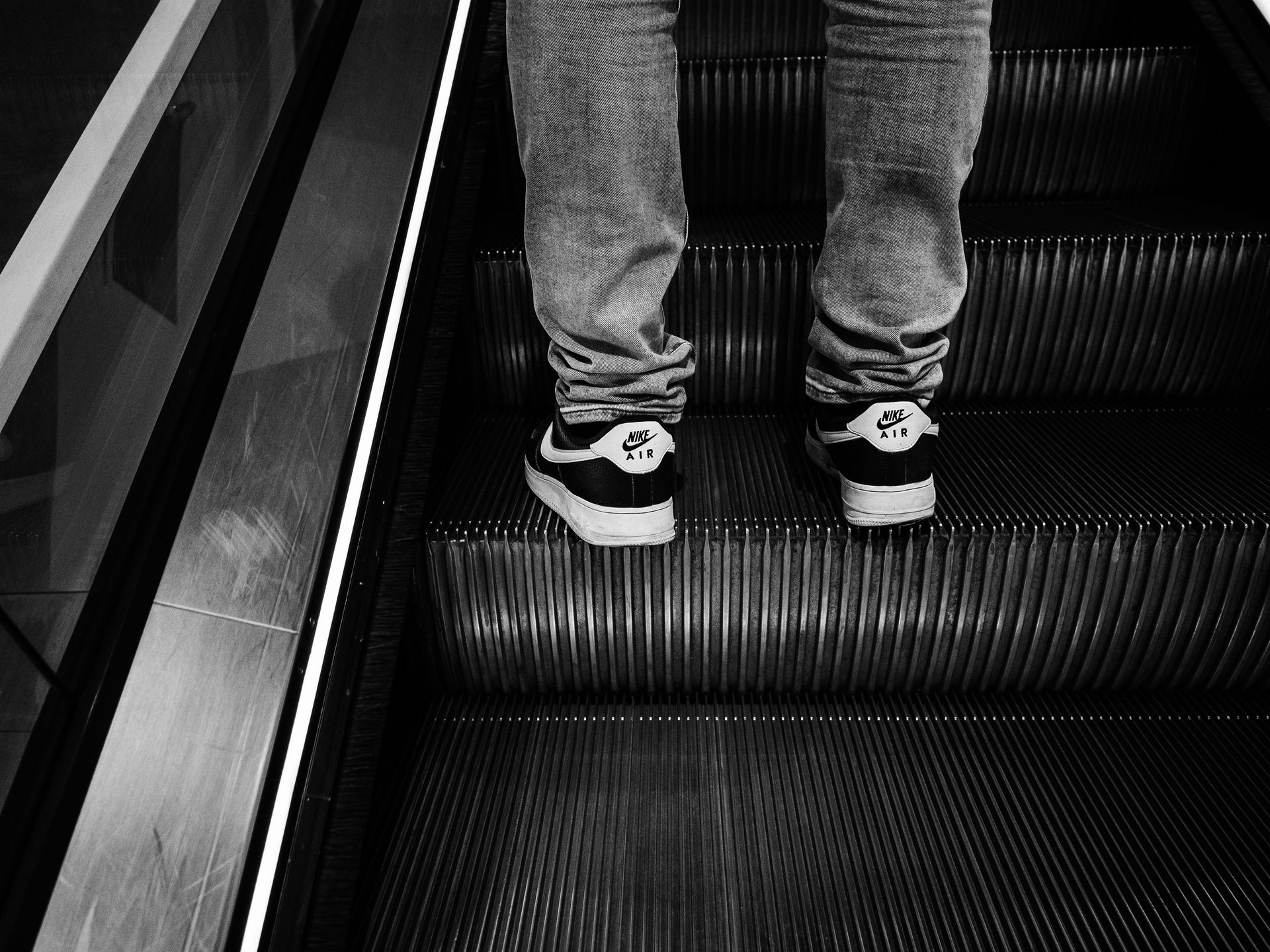 Person wearing Nike shoes on an escalator A black and white photo of a person 's feet on an escalator