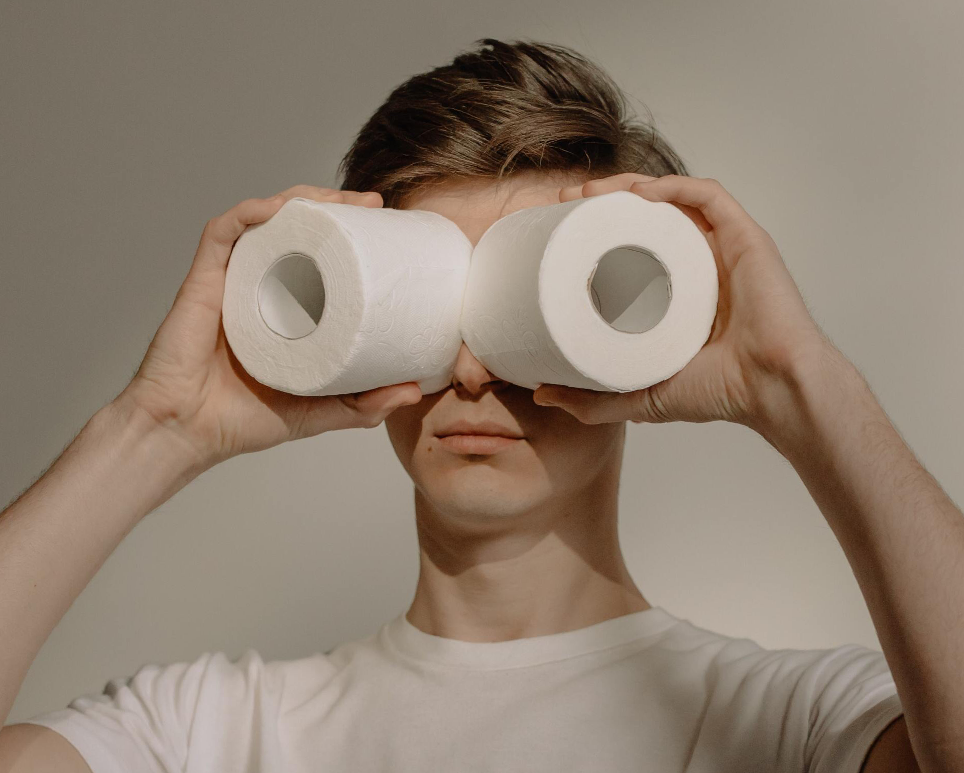 A man is holding two rolls of toilet paper in front of his eyes.
