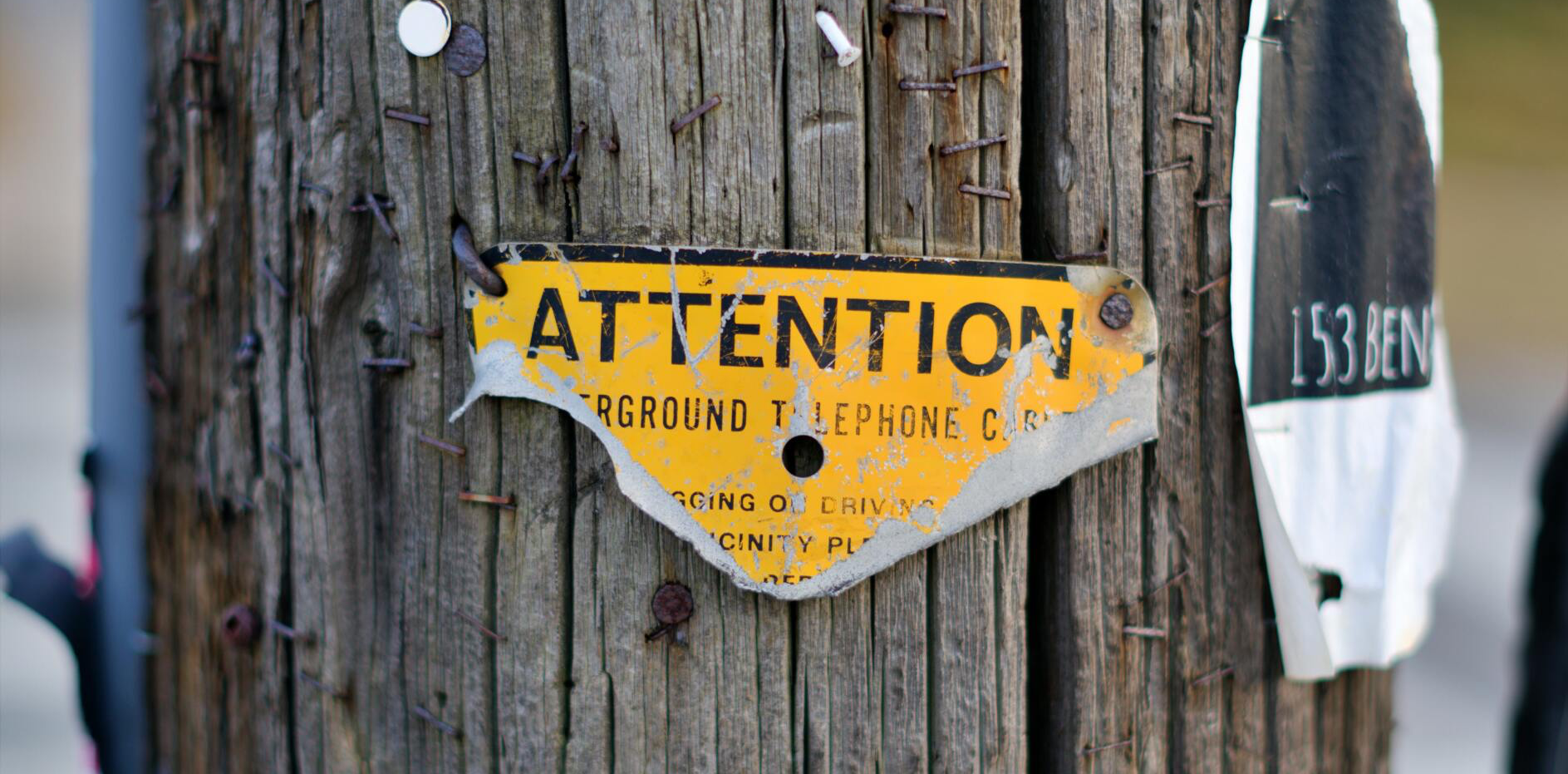 A wooden pole with a yellow sign on it that says attention