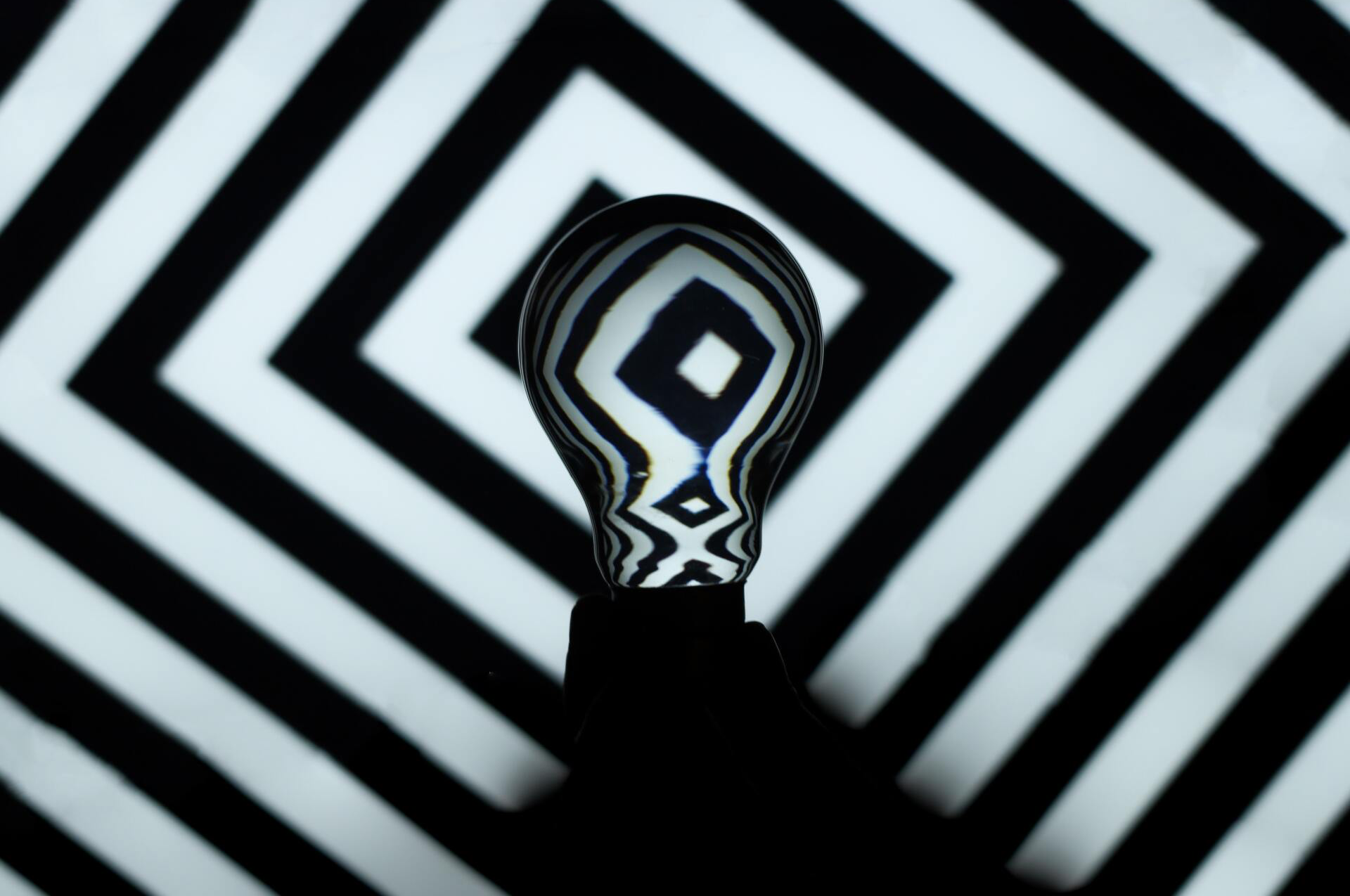 Lightbulb reflecting a black and white geometric pattern, casting a dark shadow.
