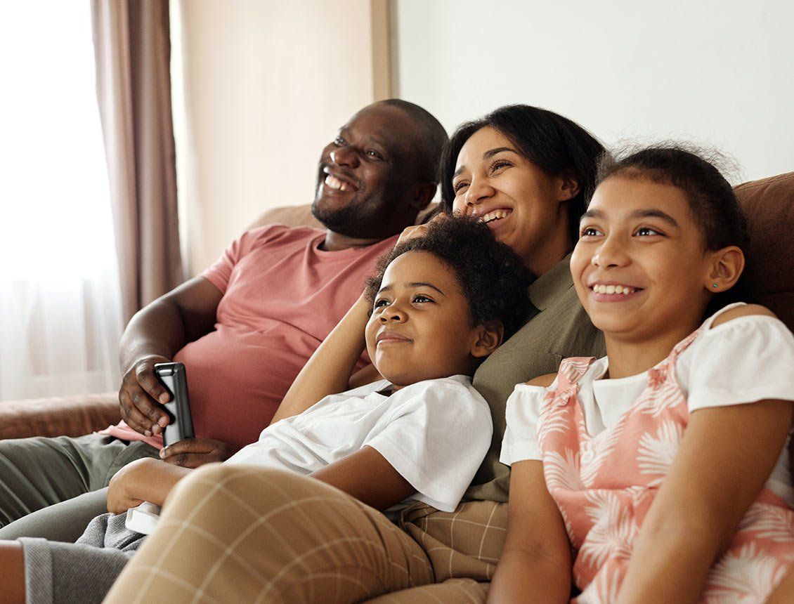 Image of family on couch watching a movie or tv A family is sitting on a couch watching tv together.
