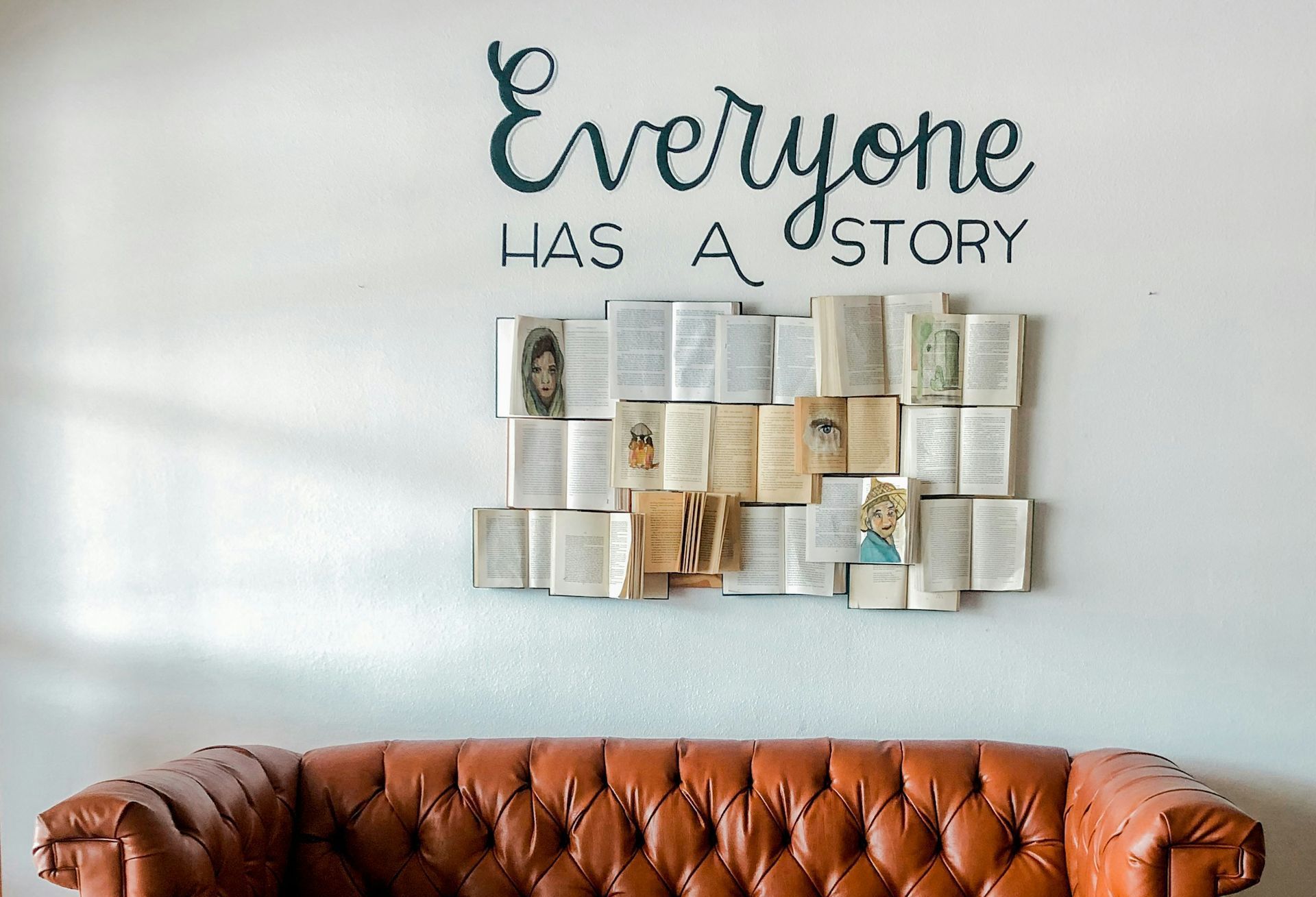 Image of wall with book and text that says A couch is sitting in front of a wall with a sign that says everyone has a story.