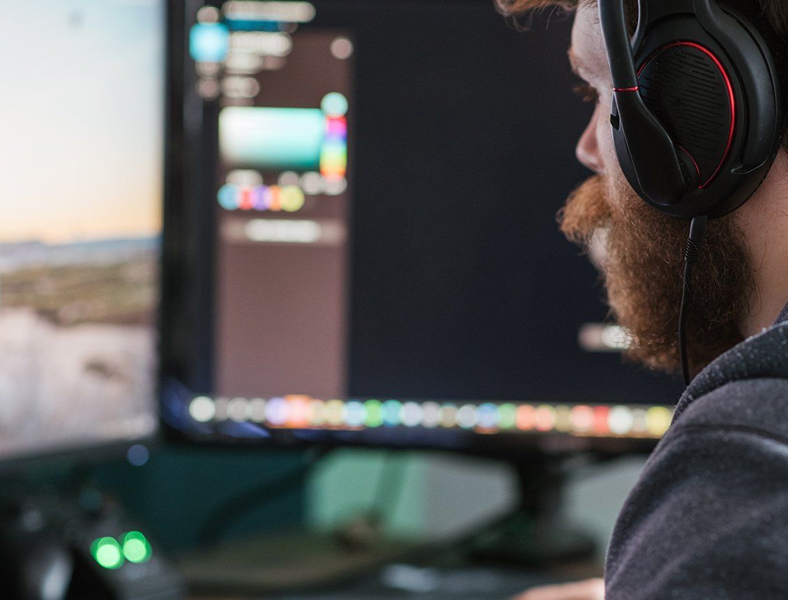 Close up video editor with beard and wearing headphones A man wearing headphones is looking at a computer screen.