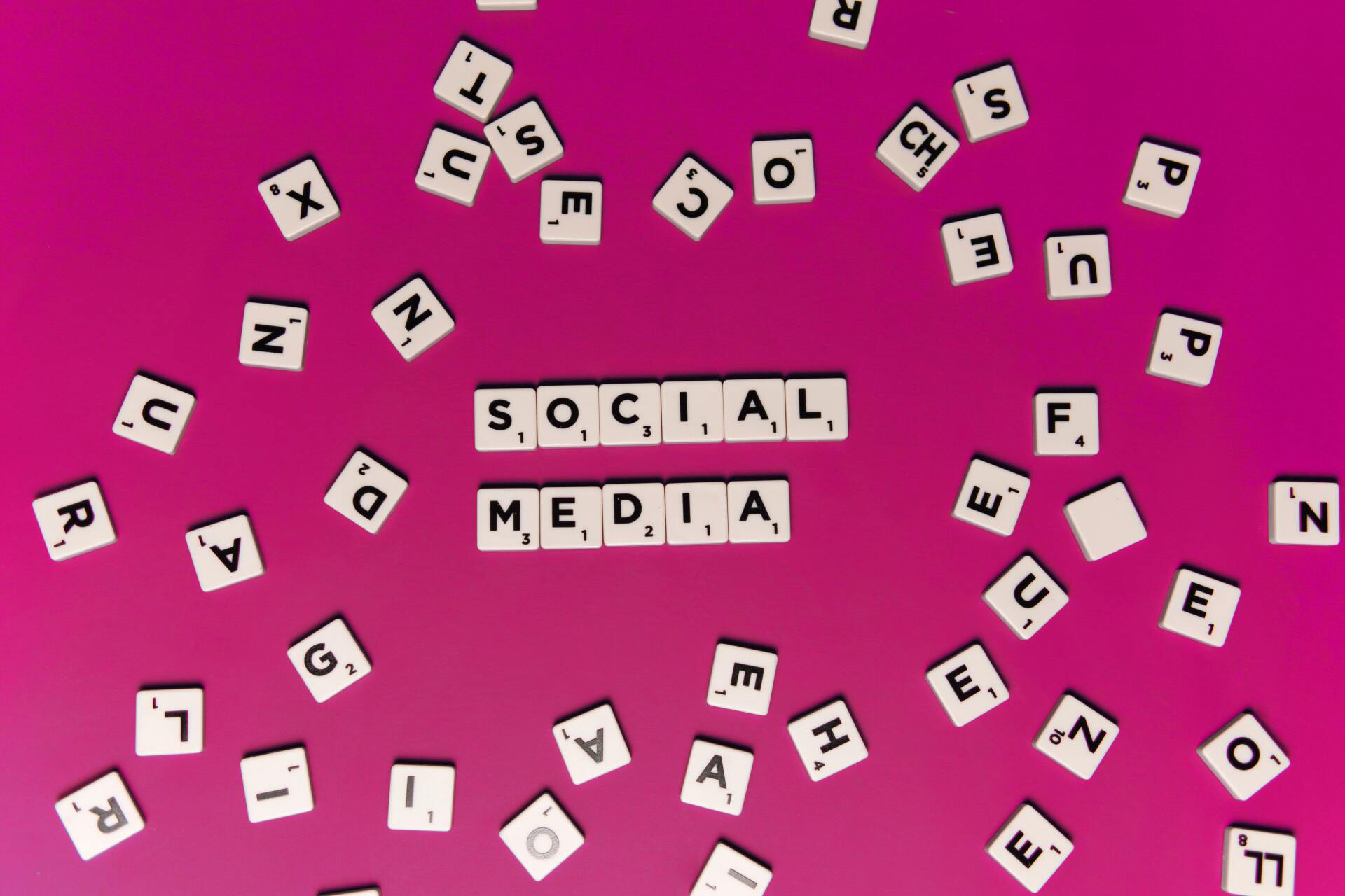 The word social media is written in scrabble tiles on a pink background