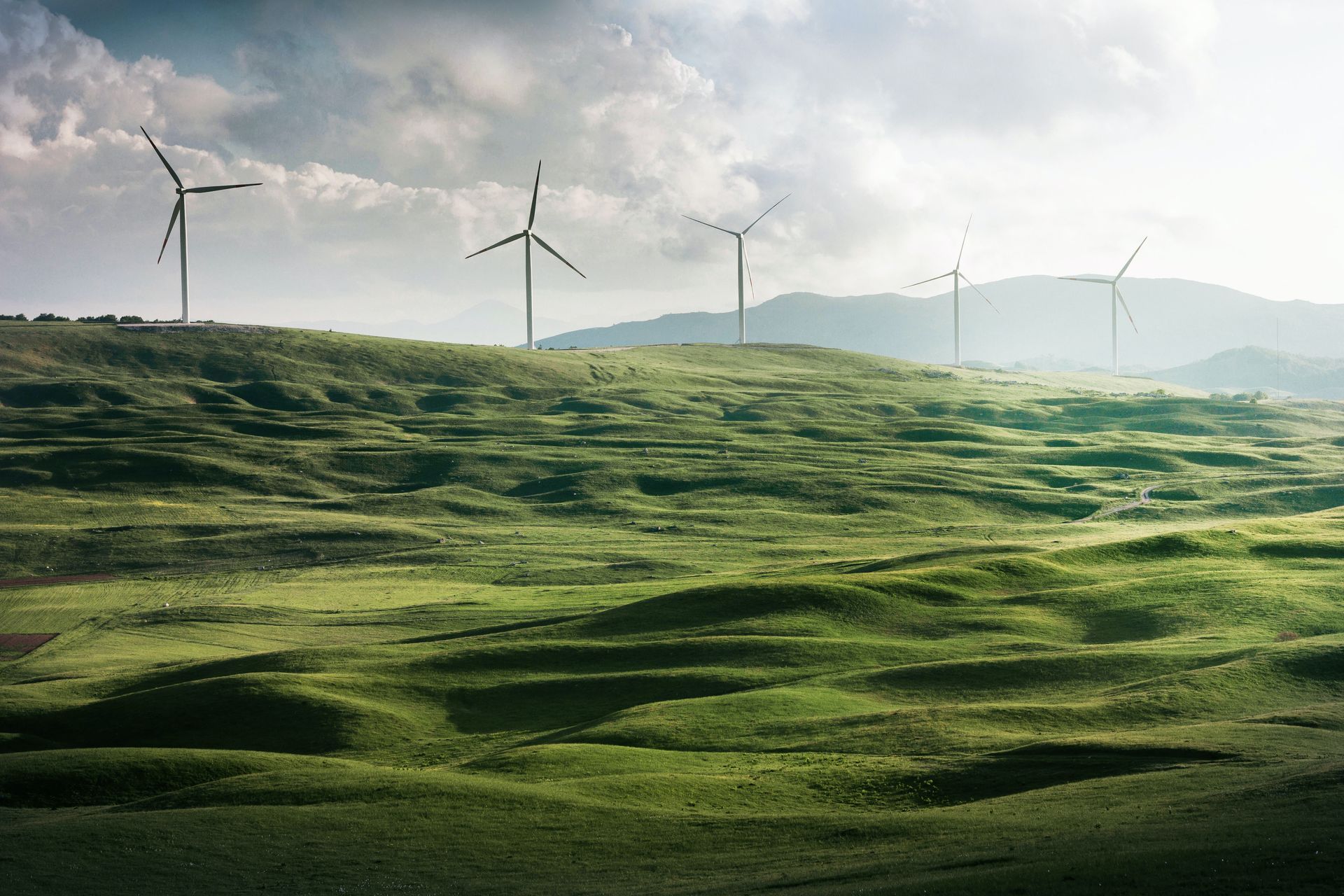 Windmills at the top of a rolling green pasture A row of wind turbines are sitting on top of a grassy hill.