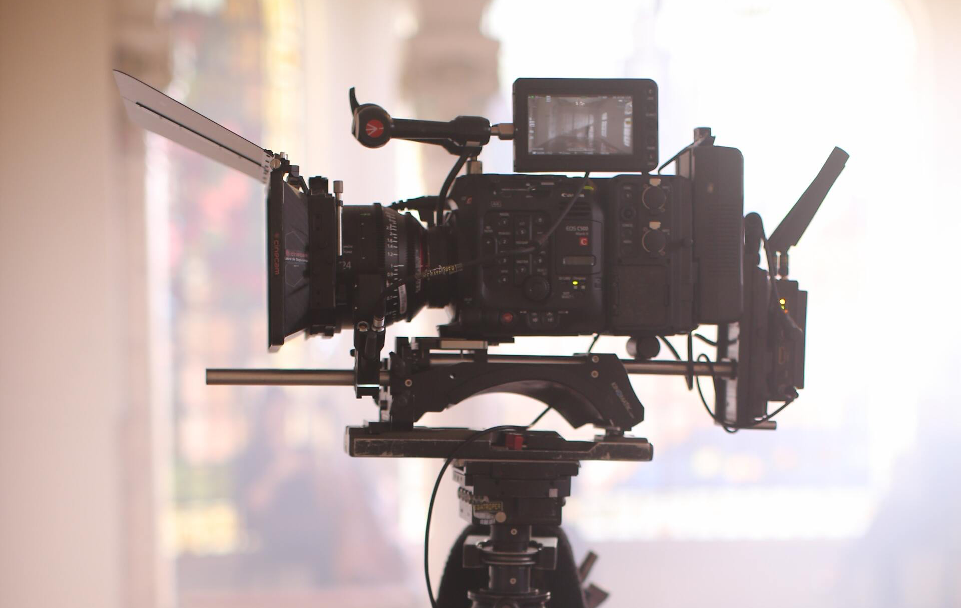 A camera is sitting on a tripod in front of a window.