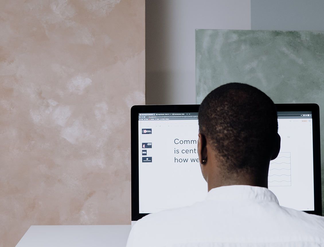 A man in a white shirt is sitting in front of a computer monitor.