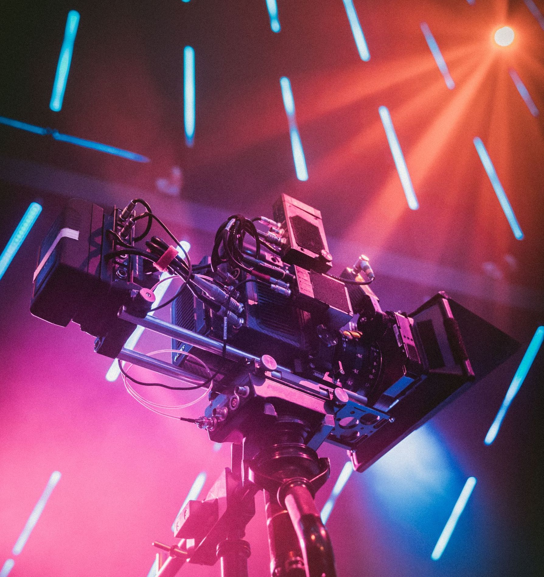 A camera on a tripod with purple and blue lights behind it