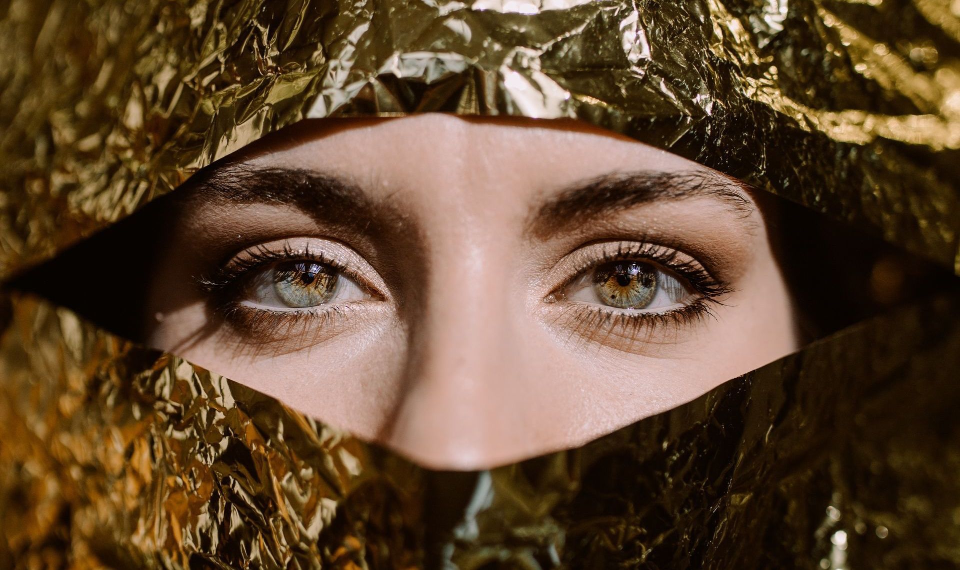 A close up of a woman 's face covered in gold foil.
