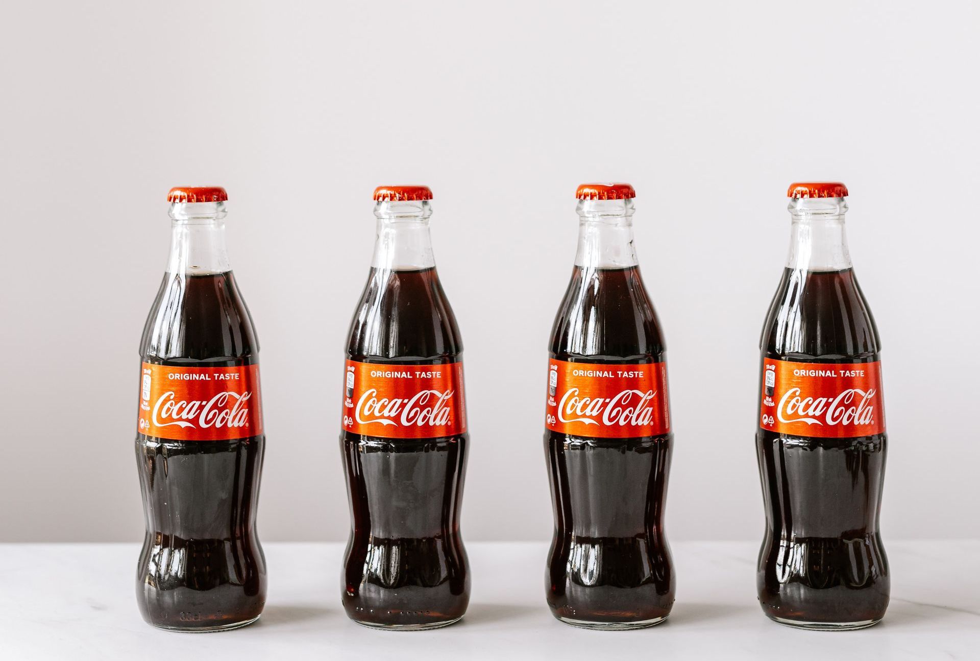 Four bottles of coca cola are lined up on a table.
