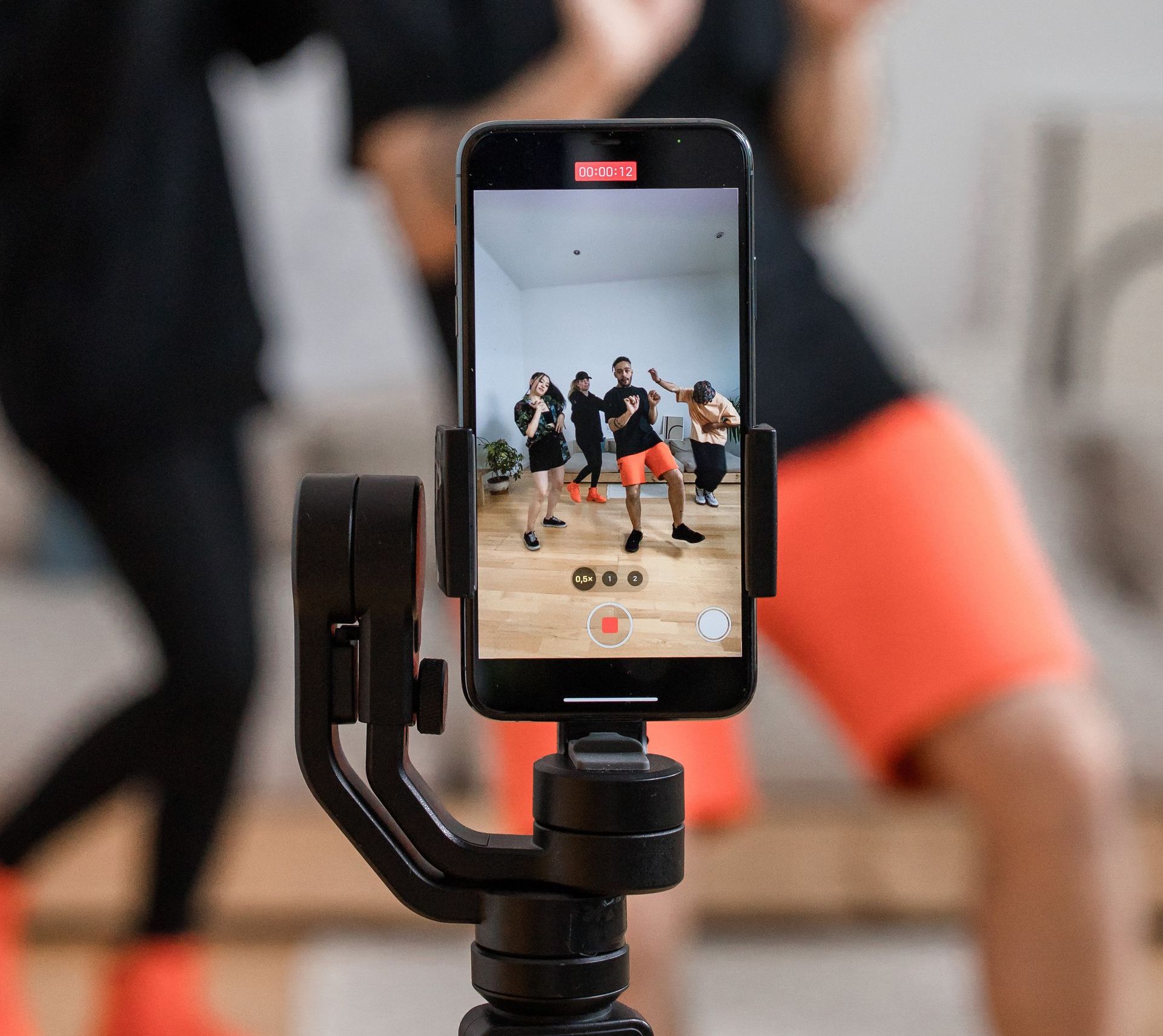 Smartphone recording dance class, set on a tripod. Dancers in black and orange outfits.