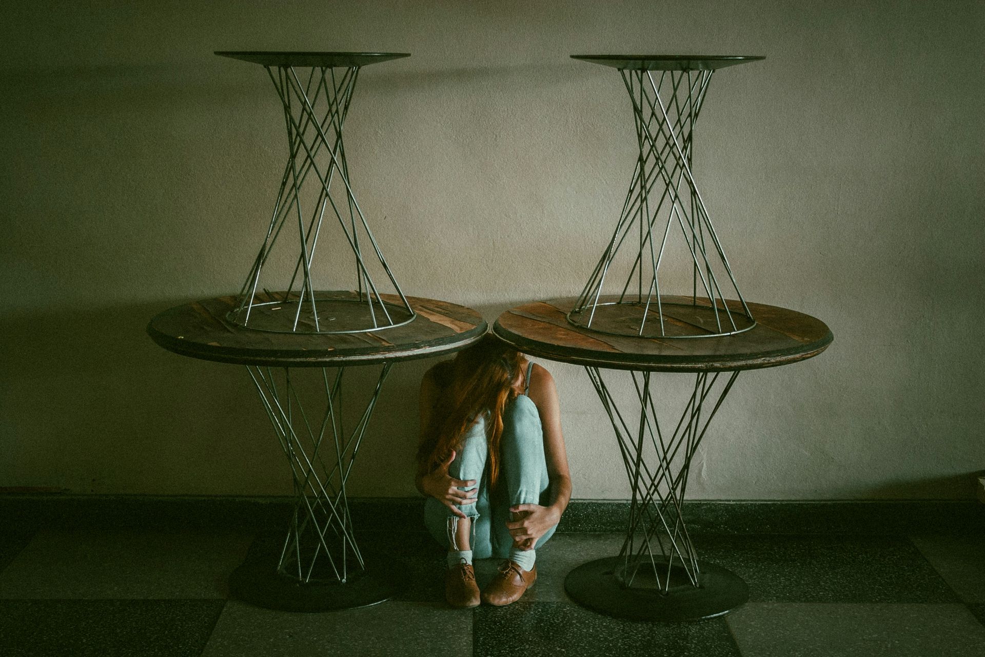 Person crouched between two spiral-legged tables; interior setting, neutral tones. Person crouched between two spiral-legged tables; interior setting, neutral tones.