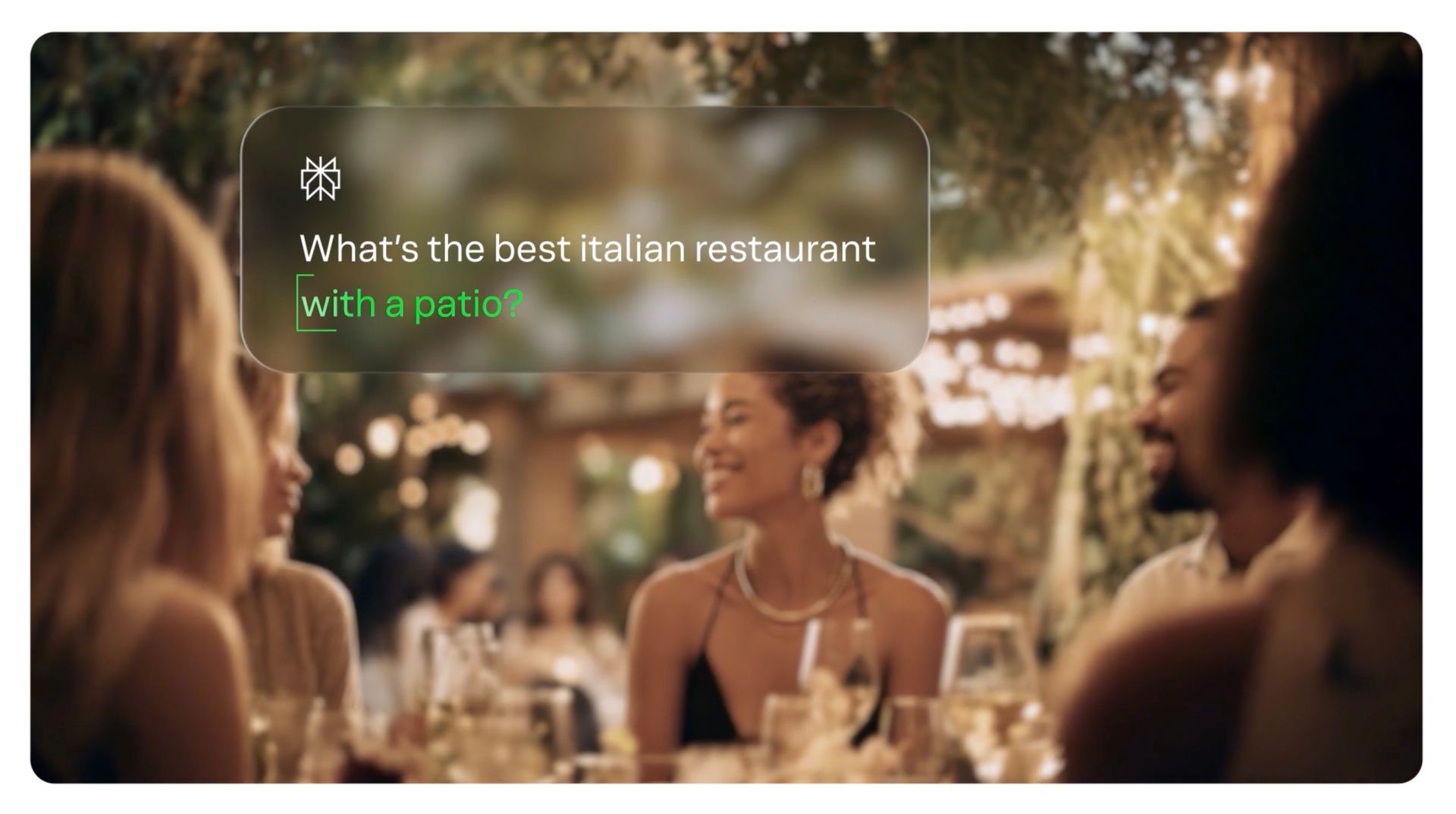 Outdoor dinner party with people seated around a table under warm string lights, with a text overlay about the best Italian restaurant, from the Yext Be the Answer brand film.