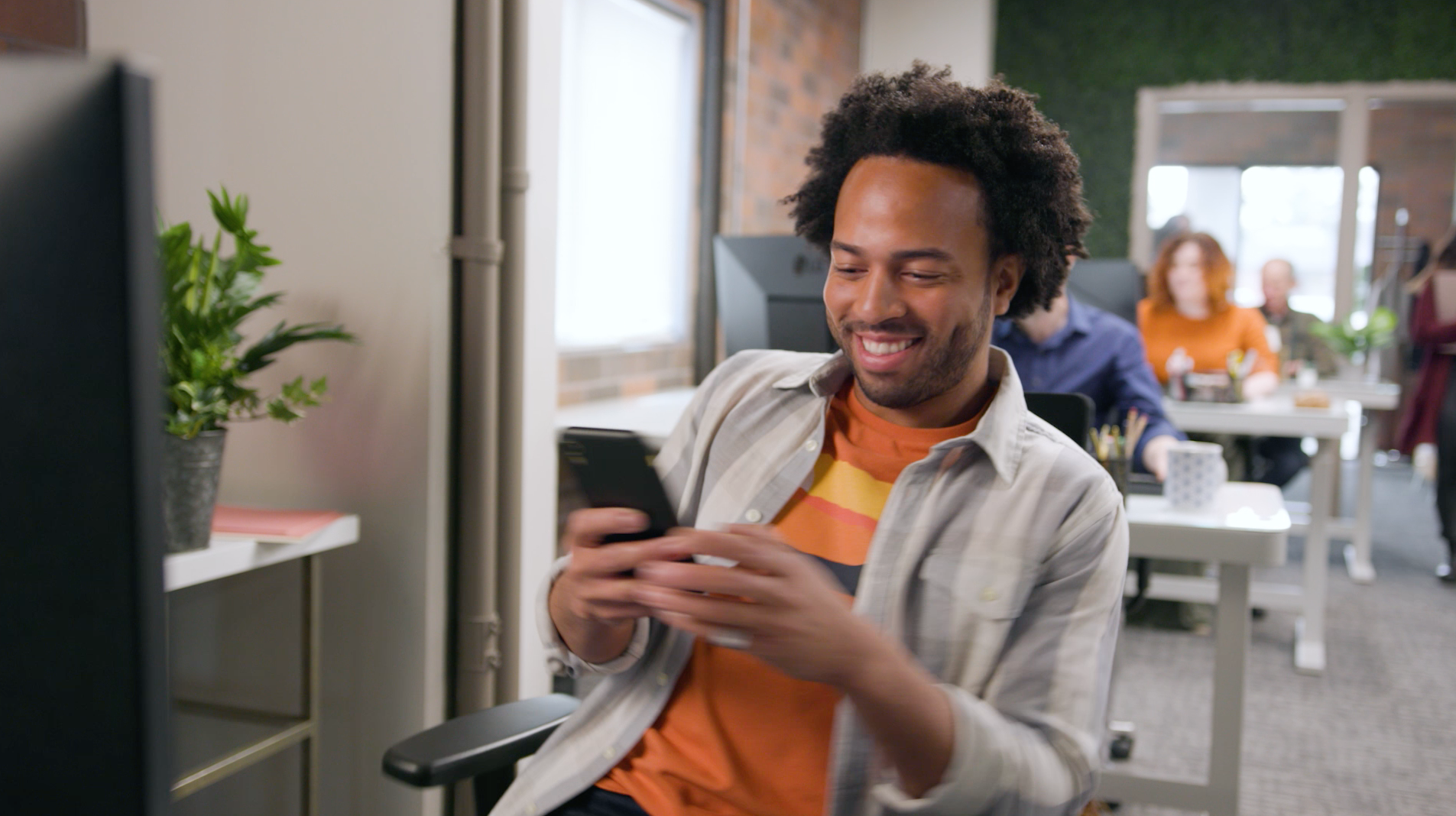 A man is sitting in an office chair looking at his cell phone.