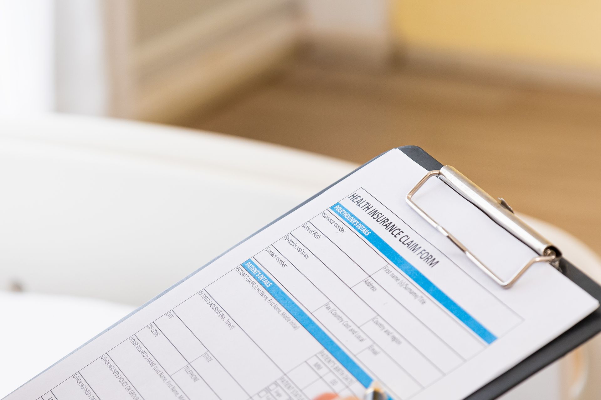 Clipboard with a health insurance claim form, held in a room with a white medical chair.