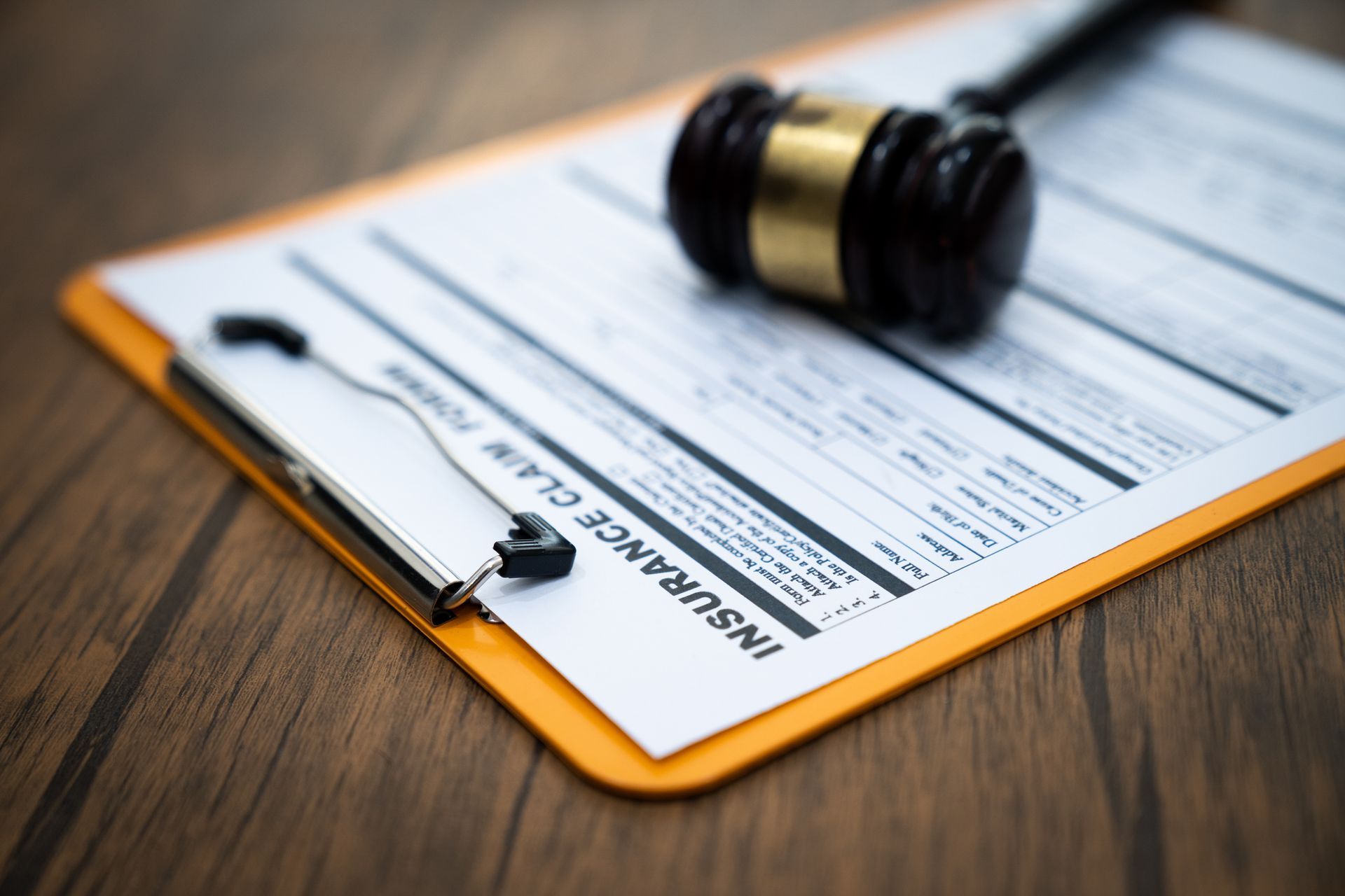 Gavel rests on insurance claim form on clipboard, wooden table background. Gavel rests on insurance claim form on clipboard, wooden table background.