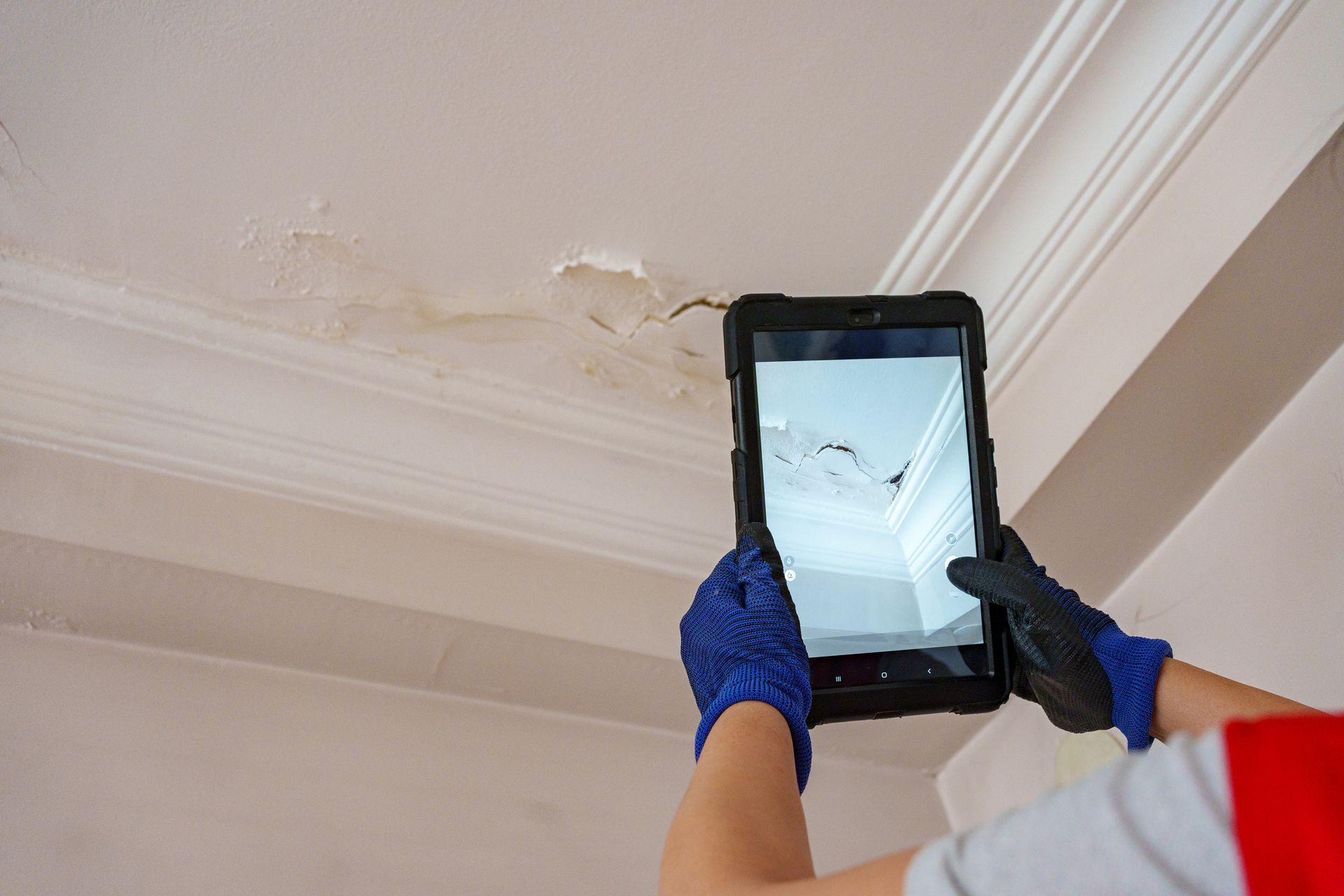 Person in blue gloves using tablet to document ceiling water damage. Person in blue gloves using tablet to document ceiling water damage.