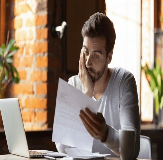 Man looking stressed while reading papers near a laptop and coffee cup; indoor setting. Man looking stressed while reading papers near a laptop and coffee cup; indoor setting.