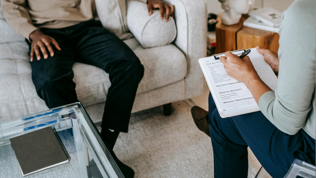 Therapist and client in a counseling session, with clipboard notes and coffee table in a living room.