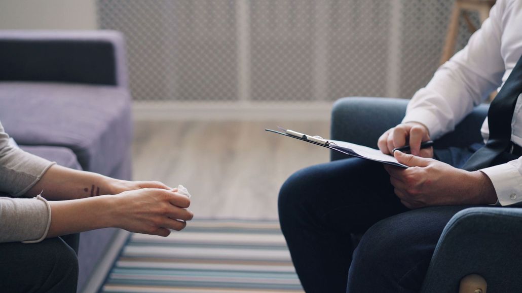 Two people seated in a meeting, one holding a notepad and the other gesturing with a pen.