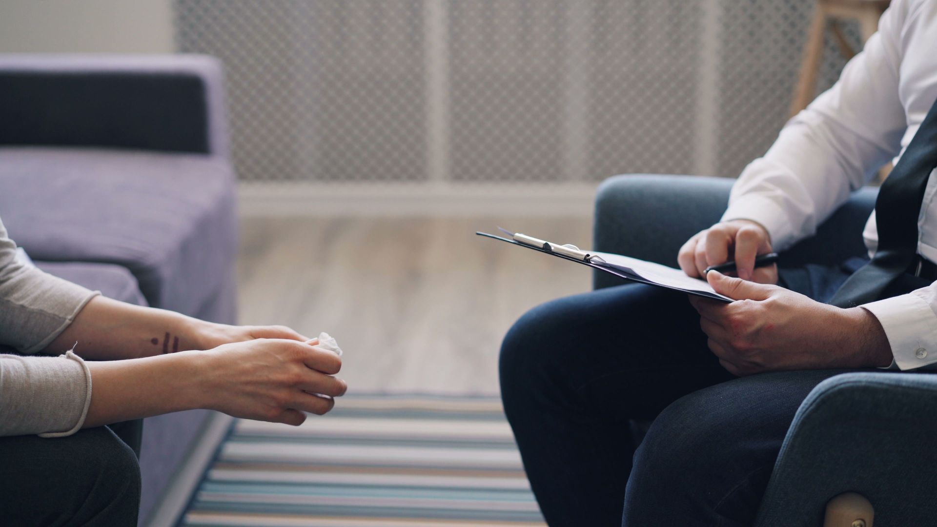 Two people seated in a meeting, one holding a notepad and the other gesturing with a pen.