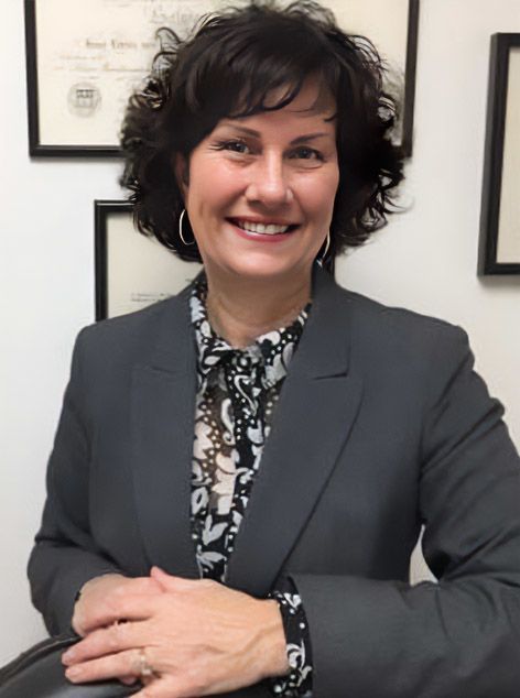 Woman in a gray blazer smiling with arms crossed in an office setting