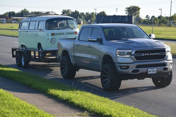Teal vintage van on a trailer hitched to a gray pickup truck on a sunny roadside