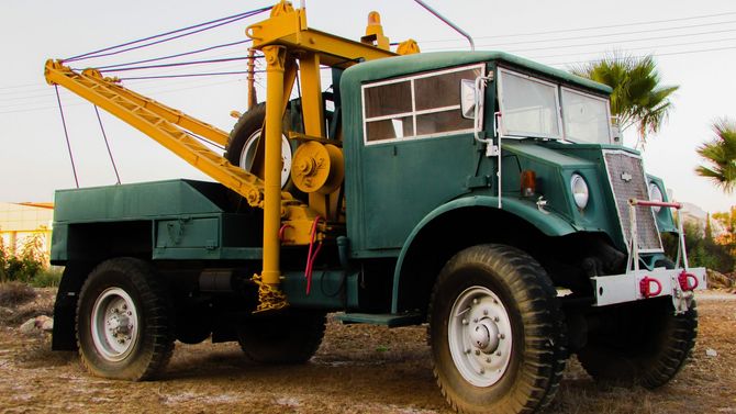 Green tow truck with yellow crane arm parked outdoors on a dirt lot.