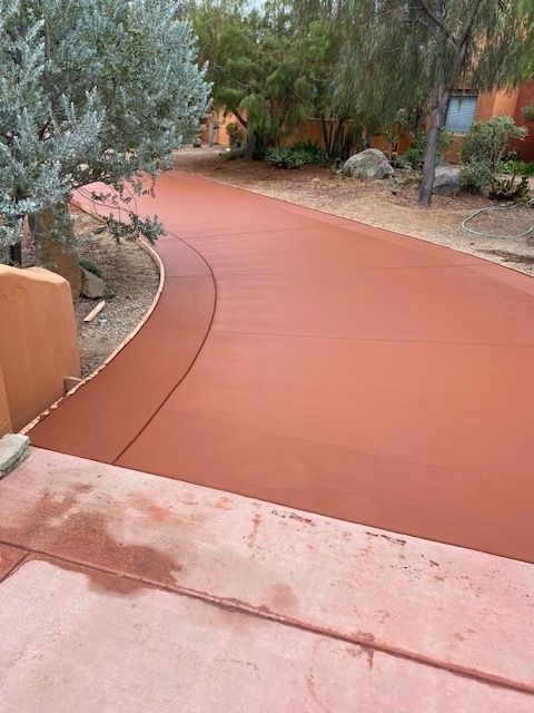 A red concrete driveway with trees on the side of it.