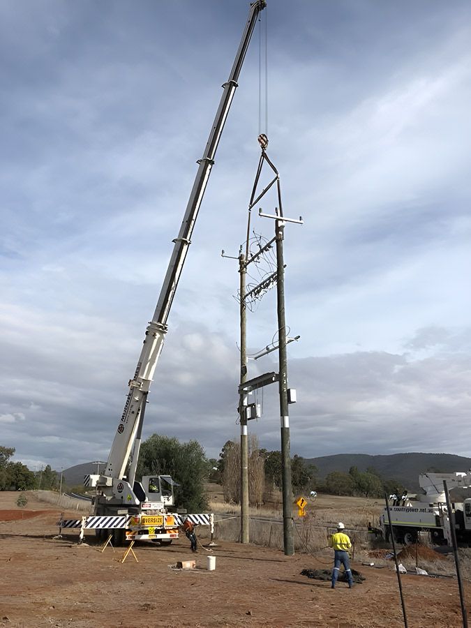 A Crane is Lifting a Telephone Pole in a Dirt Field — Country Powerline Constructions in Bourke, NSW