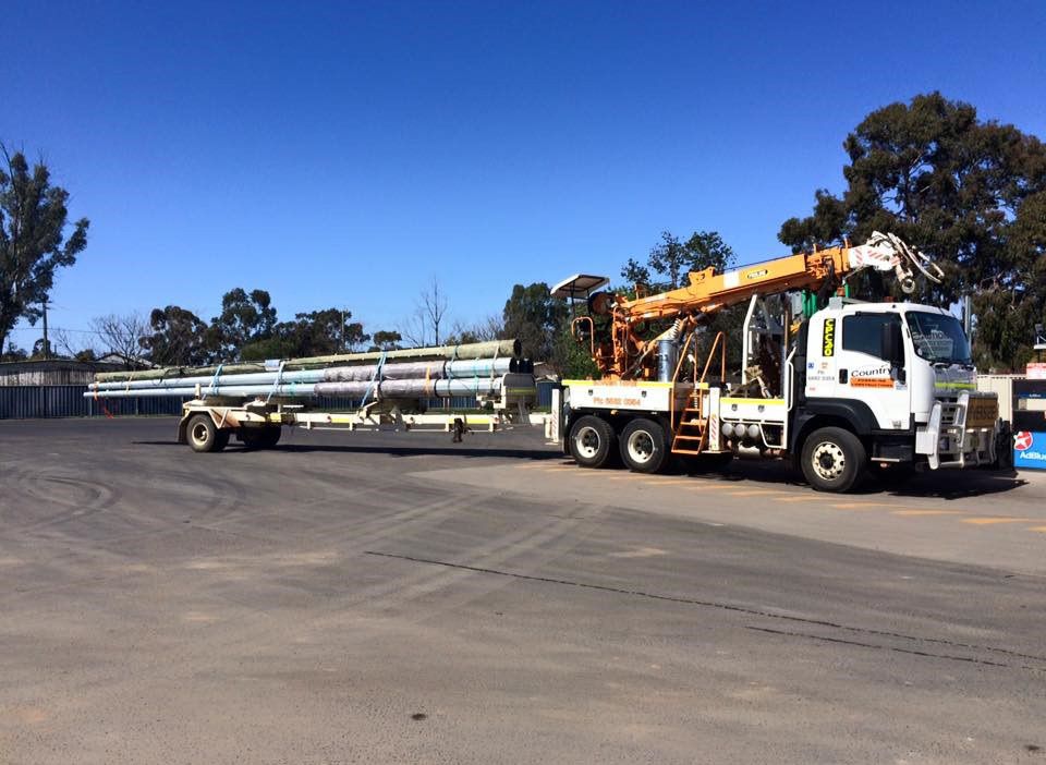 A Truck is Carrying a Trailer With Pipes on It — Country Powerline Constructions in Condoblin, NSW
