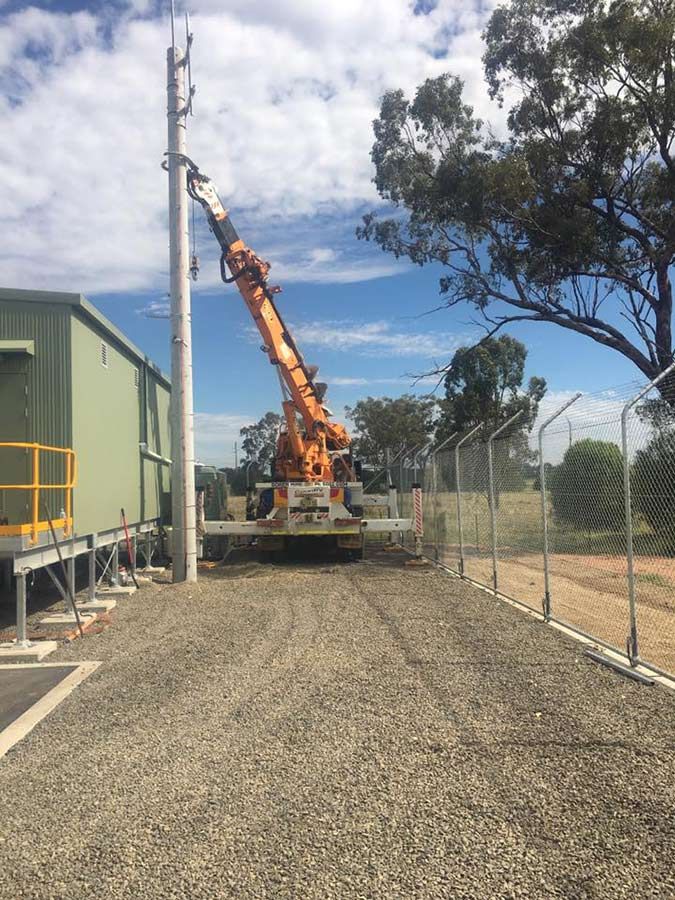 A Crane is Sitting on Top of a Gravel Road Next to a Fence — Country Powerline Constructions in Dubbo, NSW