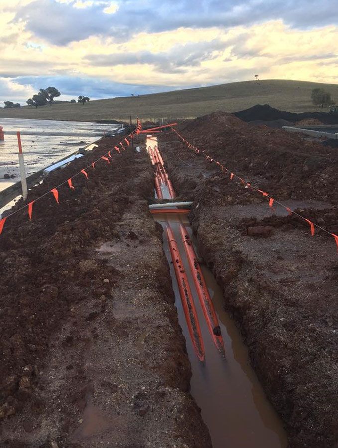 A Muddy Trench With Orange Flags on the Side of It — Country Powerline Constructions in Condoblin, NSW
