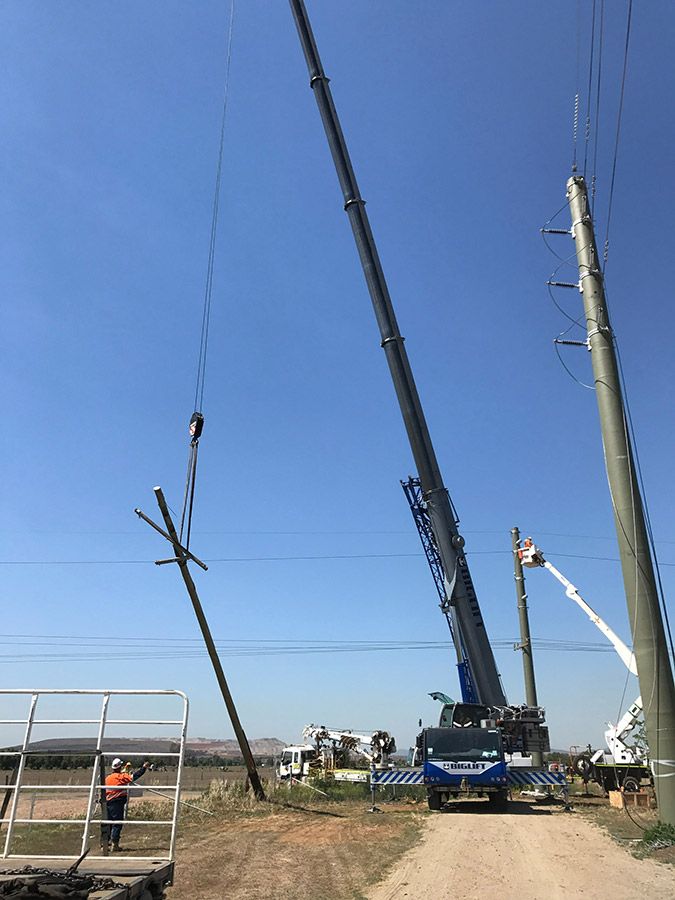 A Crane is Lifting a Telephone Pole on a Dirt Road — Country Powerline Constructions in Forbes, NSW