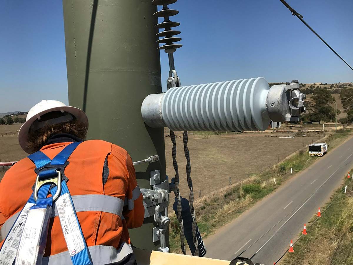 A Man Wearing a Hard Hat and Safety Harness is Working on a Power Line — Country Powerline Constructions in Orange, NSW