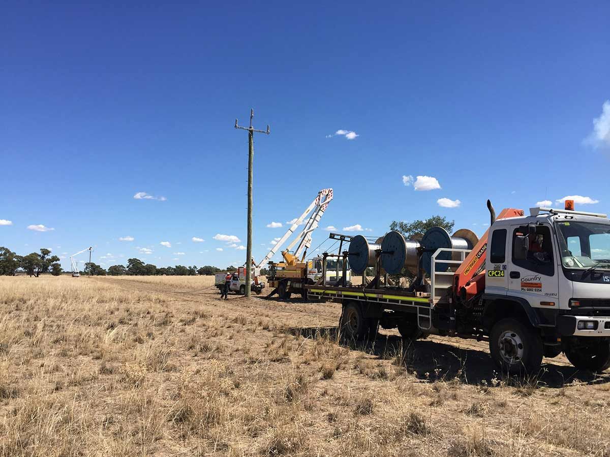 A Truck With a Crane on the Back of It is Parked in a Field — Country Powerline Constructions in Dubbo, NSW
