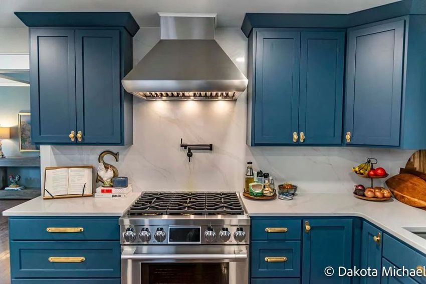 Blue kitchen with stainless steel stove and hood, white backsplash, and countertops with fruit and decor.