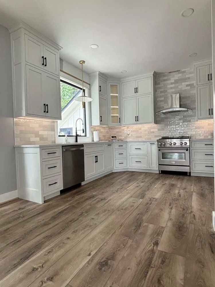 Modern white kitchen with stainless appliances, wood-look floors, and a large window over the sink