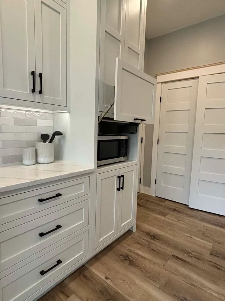 White kitchen with built-in microwave, cabinets, drawers, and wood flooring